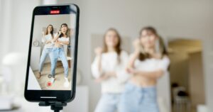 Two women dance in front of a smartphone camera, recording content indoors.